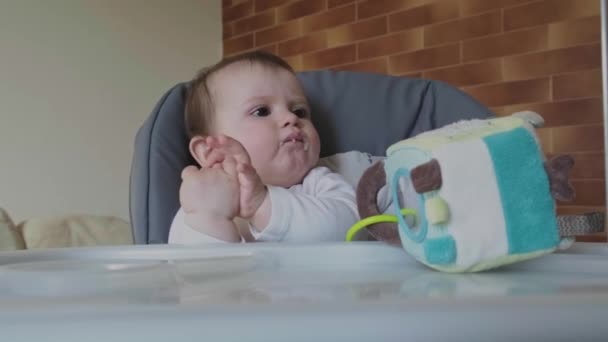 Bebé masticando comida mirando hacia otro lado mientras juega con sus manos sentadas en la trona. Alimentación saludable. Bebé comida de mañana. — Vídeo de stock