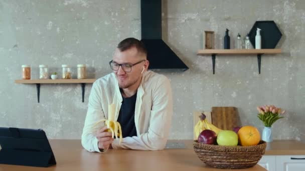 Καυκάσιος επιχειρηματίας μιλάει με τους συναδέλφους του για μια επιχείρηση σε ένα βίντεο-συνέδριο. Τρώω μπανάνες. Για σχεδιασμό τρόπου ζωής. Τεχνολογία Διαδικτύου. Βίντεο — Αρχείο Βίντεο