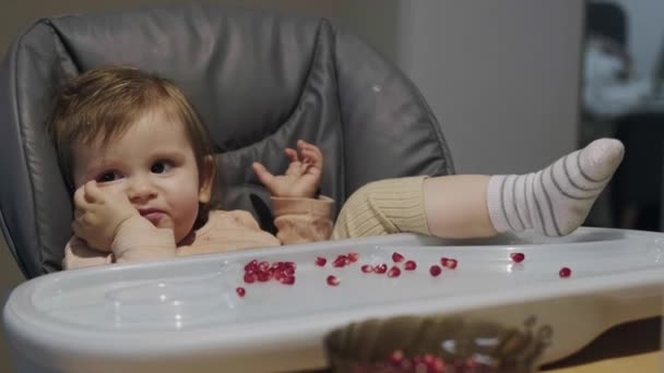 Bébé fille assis confortablement dans une chaise haute et bâillant après une collation saine grenade. Expression faciale. Une nourriture saine. Manger des grenades. — Video