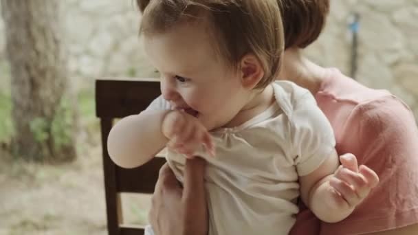 Bebek torununu kollarında tutan bir büyükannenin yakın plan portresi. Bebek parmaklarını ağzına sokuyor. Aile günü. Mutlu insanlar.. — Stok video