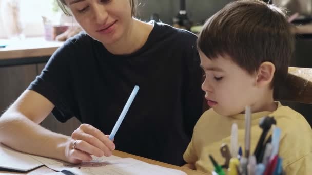 Mamãe sentada com o filhinho na mesa fazendo lição de casa explicando o exercício que ele não entendia. Retrato de perto. Tempo de aprendizagem. — Vídeo de Stock