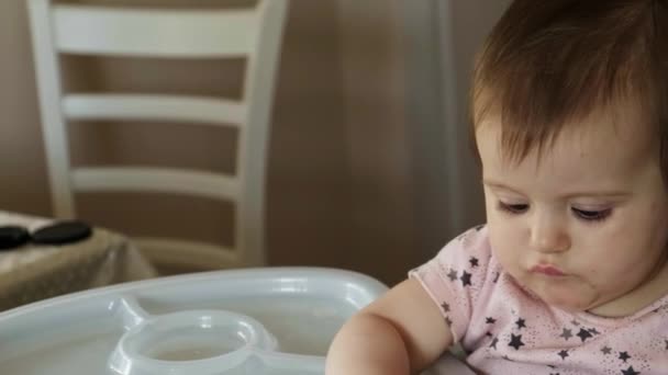Közelkép egy magasszékben ülő babáról, amint gyümölcsöt vesz ki az asztalról, és beleharap az étvágyával. Arckifejezés. Bioélelmiszerek. — Stock videók