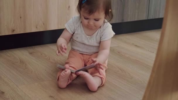 Baby zittend op een vloer met een boekje, spelend terwijl hij op zijn rug viel en dan liggend op zijn buik. Een energiek kind. Kinderontwikkeling. Baby ontwikkeling — Stockvideo