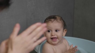 Anne elleri, küvette banyo yaparken küçük kıza ellerini nasıl yıkayacağını gösteriyor. Sağlıklı saçlar.