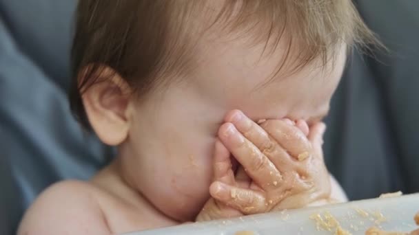 Το χέρι της μητέρας ταΐζει το βρώμικο μωρό από το στόμα που κάθεται στην ψηλή καρέκλα, κορεσμένο από τόσο φαγητό. Η μητέρα σκουπίζει το βρώμικο πρόσωπο των μωρών. Φροντίδα μωρών — Αρχείο Βίντεο