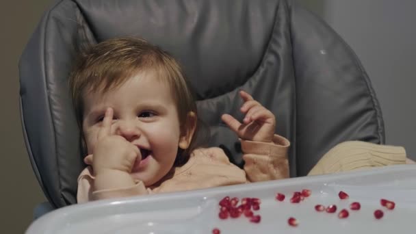 Porträt eines glücklichen jungen Mädchens im Hochstuhl mit Granatapfelkernen auf dem Tisch. Lächelndes glückliches Kind. Bio-Lebensmittel. Süßes Essen. — Stockvideo