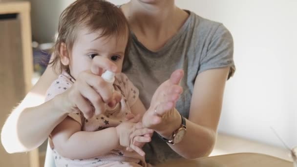 Retrato de cerca de una madre usando un biberón antiséptico para desinfectar sus manos y las manos del bebé que sostiene. Concepto de higiene. — Vídeos de Stock