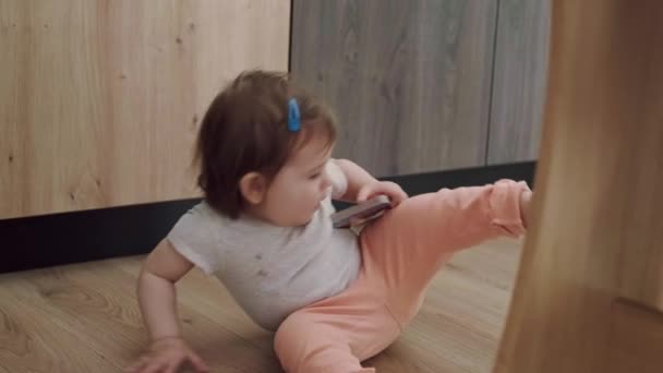 La niña sentada en el suelo en la habitación sosteniendo un juguete y acostada boca abajo. Sonriente niña feliz. Estilo de vida saludable. — Vídeos de Stock