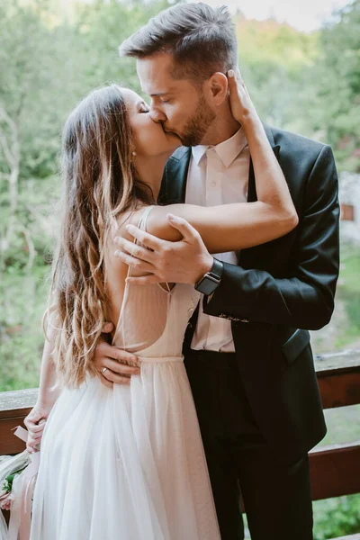 Noiva e noivo beijando enquanto estava na varanda de uma casa de campo de madeira na floresta. Retrato de close-up. Incrível natureza verão. — Fotografia de Stock