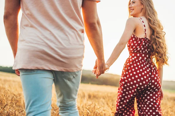 Bakifrån av ett lyckligt par som håller händerna gående genom en äng. Vetefält. Vacker ung flicka. — Stockfoto
