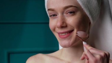 Yüzüne masaj yapmak için yeşim taşı kullanan bir kadının yakın plan portresi. Zevkle gülümsüyor. Dermatoloji, kozmetoloji. Sağlıklı yaşam tarzı