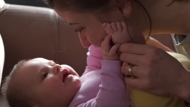 Η μητέρα φιλάει το στομάχι του κοριτσιού της ενώ παίζει με αυτό ξαπλωμένη στο κρεβάτι. Για σχεδιασμό τρόπου ζωής. Φροντίδα μωρών. — Αρχείο Βίντεο