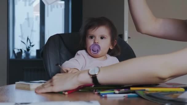 Madre che controlla le lezioni al figlio, bambina seduta in seggiolone a giocare con matite colorate. Sviluppo del bambino. Sviluppo del bambino. — Video Stock