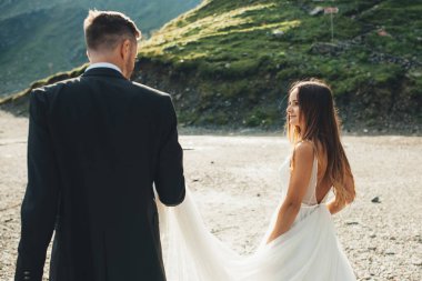 Gelin ve damat düğün günlerinde bir gölün kenarında kumda yürüyorlardı. Çift pozu.