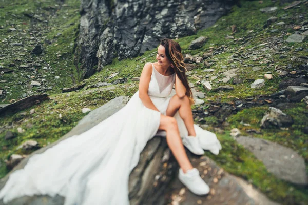 Novia con el pelo largo sentado en una piedra sobre el fondo de rocas y acantilados, y mirando a un lado. Modelo de moda. —  Fotos de Stock