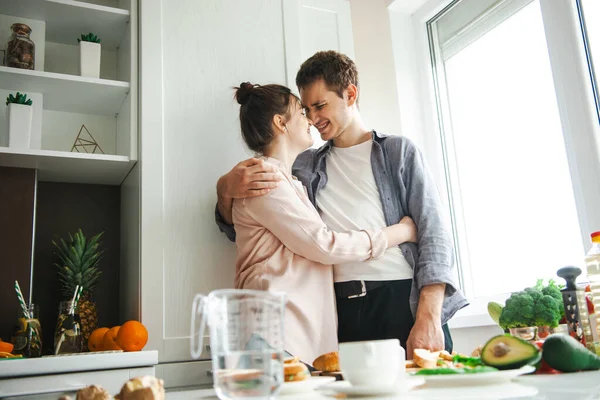 Egy pár ölelkezik, miközben a konyhában állnak és reggelit akarnak készíteni. Főzés, együtt, konyha, kapcsolat. Egészséges étel. Tevékenységi viszony — Stock Fotó