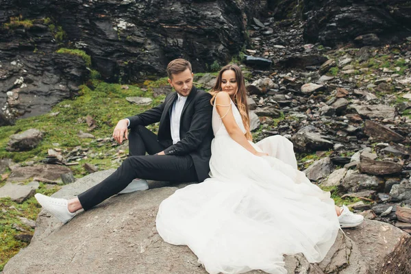 Portret pary robiącej sesję zdjęciową w dniu ślubu siedzącej na kamiennym grzbiecie na tle skalistego górskiego wzgórza. Piękny portret — Zdjęcie stockowe