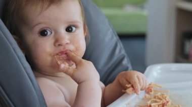 Bebek kız kameraya bakıyor, kendi elleriyle domates soslu spagetti yiyor. Bebek yemek yiyor ve ortalığı dağıtıyor..
