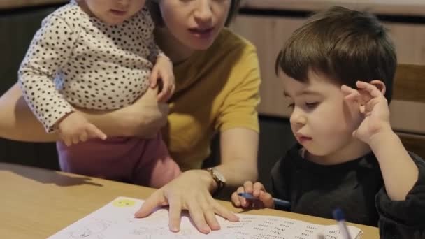 Chlapec dělá domácí úkoly s učebnicemi, kterým pomáhala jeho matka. Máma učí jeho syna. Vzdělání, rodinný životní styl, domácí výuka. Studium, dělání — Stock video