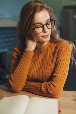 Şık kızıl kız sabahları masada oturmuş kitap okuyor. İş kadını portresi.
