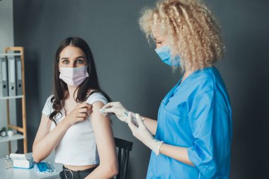 Kıvırcık saçlı doktor elinde şırıngayla kadın hastanın koluna kovid 19 aşısı yapıyor. Kadın aşı oluyor. Sağlık sigortası konsepti. Corona.