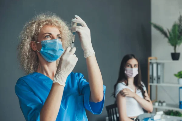 Donna caucasica con maschera facciale, che si spaventa per l'iniezione del vaccino mentre il medico prepara la siringa per vaccinare in ospedale. Per la progettazione medica. Tenersi per mano — Foto Stock