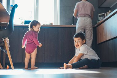 İki küçük çocuk mutfaktaki ahşap zeminde oturmuş eğleniyor. Mutlu aile.