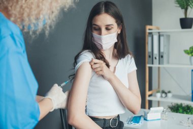 Hemşire Covid-19 aşısını yüz maskesi takan beyaz bir kadına salgın nedeniyle veriyor. Aşı konsepti. Doktor Corona 'ya virüs aşısı enjekte ediyor.