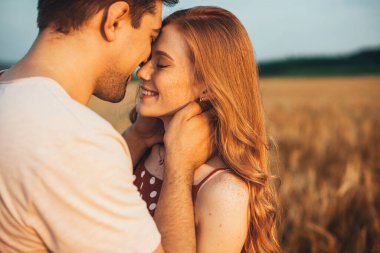 Alnına dokunan bir çift romantik ve öpüşürken arka planda bulanık bir şekilde güneşin altında poz veriyor. Aşk ve ilişkiler açık havada.