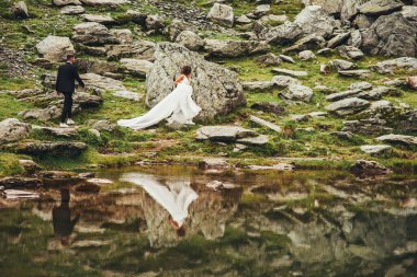 Kayalık bir göl kıyısında yürüyen yeni evliler. Doğa manzarası. Nehir kenarında zarif bir gelin ve damat. Aşık düğün çifti
