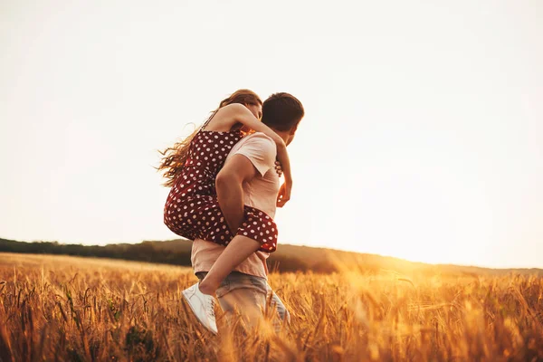 Pohledný muž vracející prasátko své přítelkyni za slunečného dne na pšeničném poli. Krásná mladá dívka. Pšeničné pole. — Stock fotografie