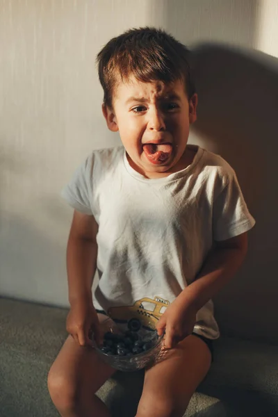 Мальчику противна отвратительная черника, которую он ест. Выражение лица. Здоровый образ жизни. Органические продукты питания. — стоковое фото