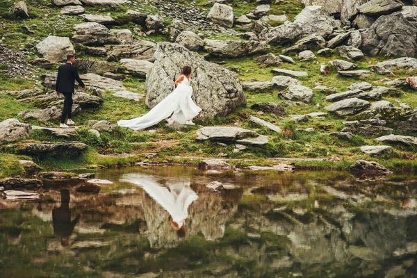 Kayalık bir göl kıyısında yürüyen yeni evliler. Doğa manzarası. Nehir kenarında zarif bir gelin ve damat. Aşık düğün çifti