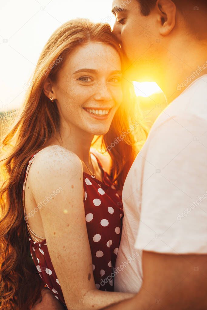 Close-up portrait of boy kissing forehead of his freckled girlfriend during autumn walk in the golden wheat field. Happy family.