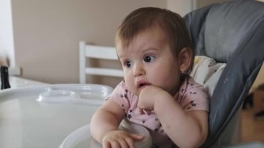 Bebek sandalyeye uzanıp yemek yemek istiyor. Anne bebeği meyvelerle besliyor. Sevimli bebek yüksek sandalyede oturuyor ve yemeye ihtiyacı var. Memnuniyetsiz çocuk...