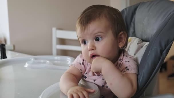 Baby girl reaching out from high-chair, wanting to eat. Mom feeding baby with fruits. Cute baby sits on high chair and needs eating. The discontented toddler is — Stock Video