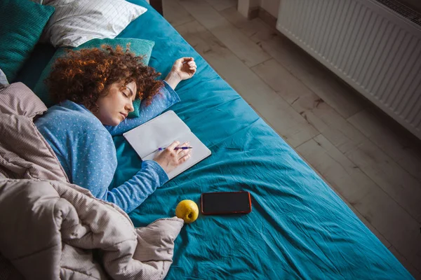 Kręcone włosy uczennica leżąca na łóżku z podręczników wokół szczęśliwie śpiąc w domu. Czas do łóżka. Koncepcja komfortu. — Zdjęcie stockowe