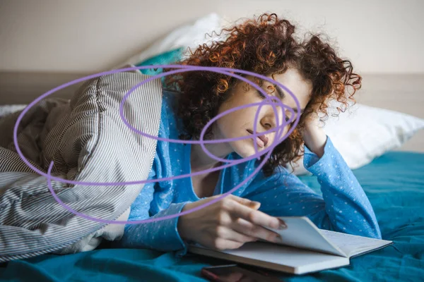 Atractiva mujer de pelo rizado acostada en la cama cubierta con manta leyendo un libro en casa. Concepto para dormir. Concepto educativo. — Foto de Stock