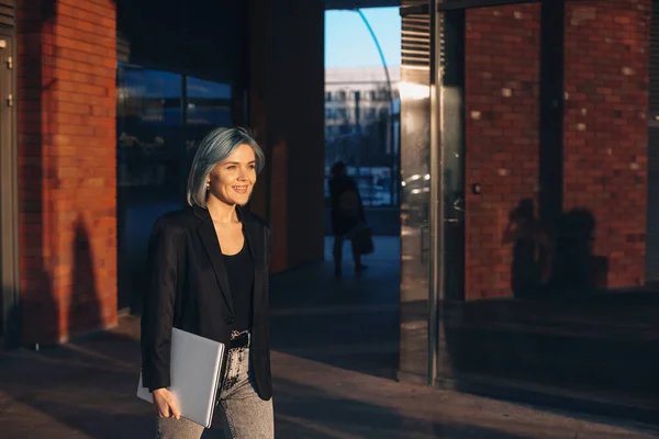 Ritratto di una donna dai capelli azzurri che tiene il computer portatile mentre cammina per strada in una giornata di sole. Ritratto da donna d'affari. Una donna che lavora al computer. Affari. — Foto Stock