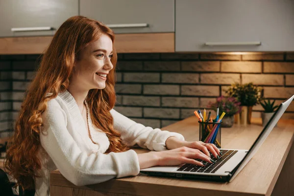 Evde çalışan kızıl saçlı kadın bilgisayarlı dizüstü bilgisayar kullanıyor konsantre olmuş ve gülümsüyor. İş kadını portresi. Çevrimiçi çalışan serbest çalışan. İnternet teknolojisi — Stok fotoğraf