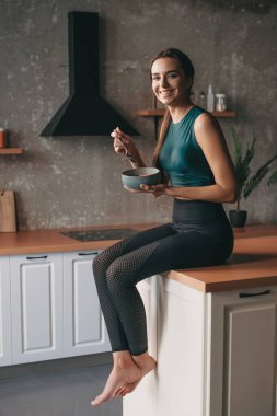 Mutfakta müsli yerken kameraya gülümseyen sportif bir kadının portresi. Sağlık hizmeti konsepti. Sağlıklı diyet kavramı.