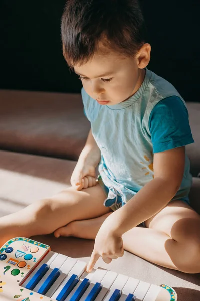 Menino sentado no chão e brincando com um piano de música de brinquedo de plástico. A divertir-se. — Fotografia de Stock