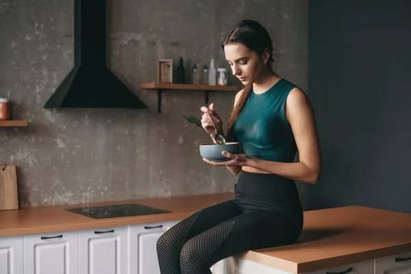 Sportif bir kadın mutfakta elinde bir kase ve kaşıkla yemek yiyor. Vejetaryen sağlıklı yiyecekler. Sağlıklı bir yaşam tarzı. Sağlıklı beslenme, diyet, kilo. — Stok fotoğraf