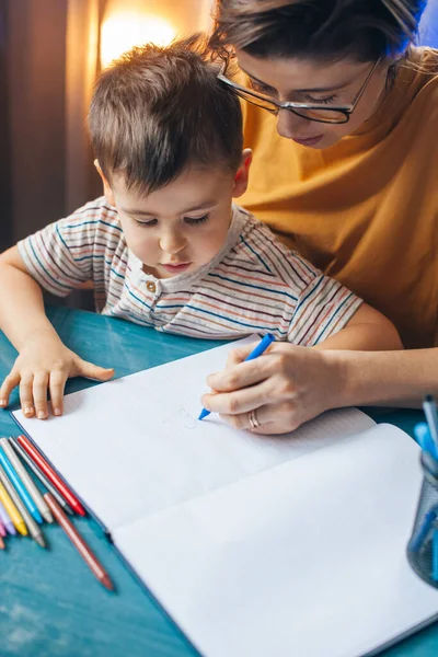 Um menino caucasiano a escrever em casa com a mãe. Tarefa de casa. Educação, aprendizagem, estudo. — Fotografia de Stock
