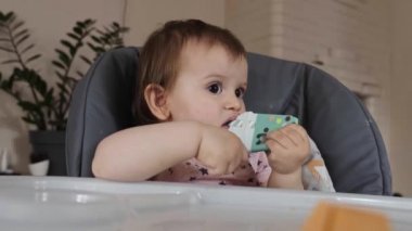 Yüksek sandalyedeki küçük kız oyuncağı ağzına oyuncak olarak koyuyor. Diş çıkarma kavramı. Bebek gelişimi. Bebek bakımı. Sağlıklı yaşam tarzı.