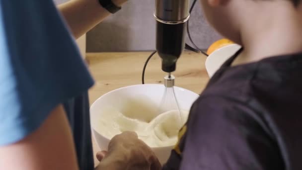 Zadní pohled na matku se synem pomocí mixéru míchat krém z mísy k narozeninovým dortům. Detailní portrét. Sladké jídlo. — Stock video