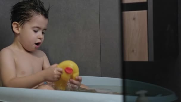 Niño caucásico tomando un baño y jugando con juguete de pato de goma con la cara sonriente. Sonriente niña feliz. Hora del baño. — Vídeos de Stock