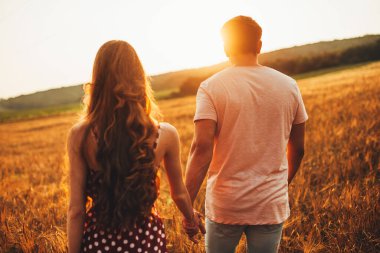 Rear view of girls and a guy in a wheat field walking holding hands looking forward. Wheat field. Holding hands. Healthy lifestyle.