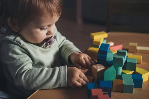Cute baby girl sitting in high-chair and building tower of colorful cubes toy. Baby care. — стоковое фото