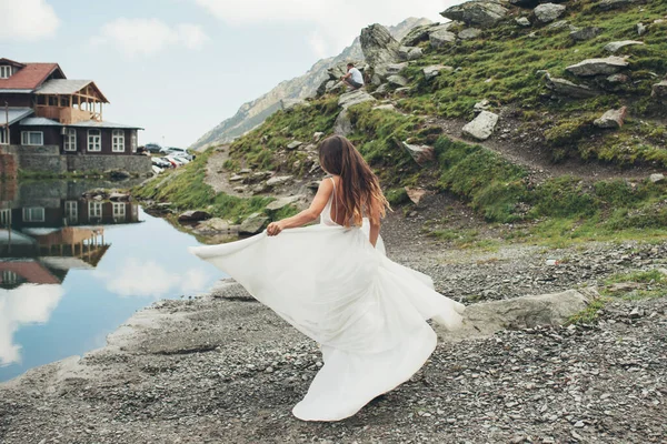 Rückenansicht einer Braut, die im weißen Brautkleid am Ufer des Sees spaziert. Schöne Sommerlandschaft. Meereslandschaft. Schöne Mädchen. — Stockfoto